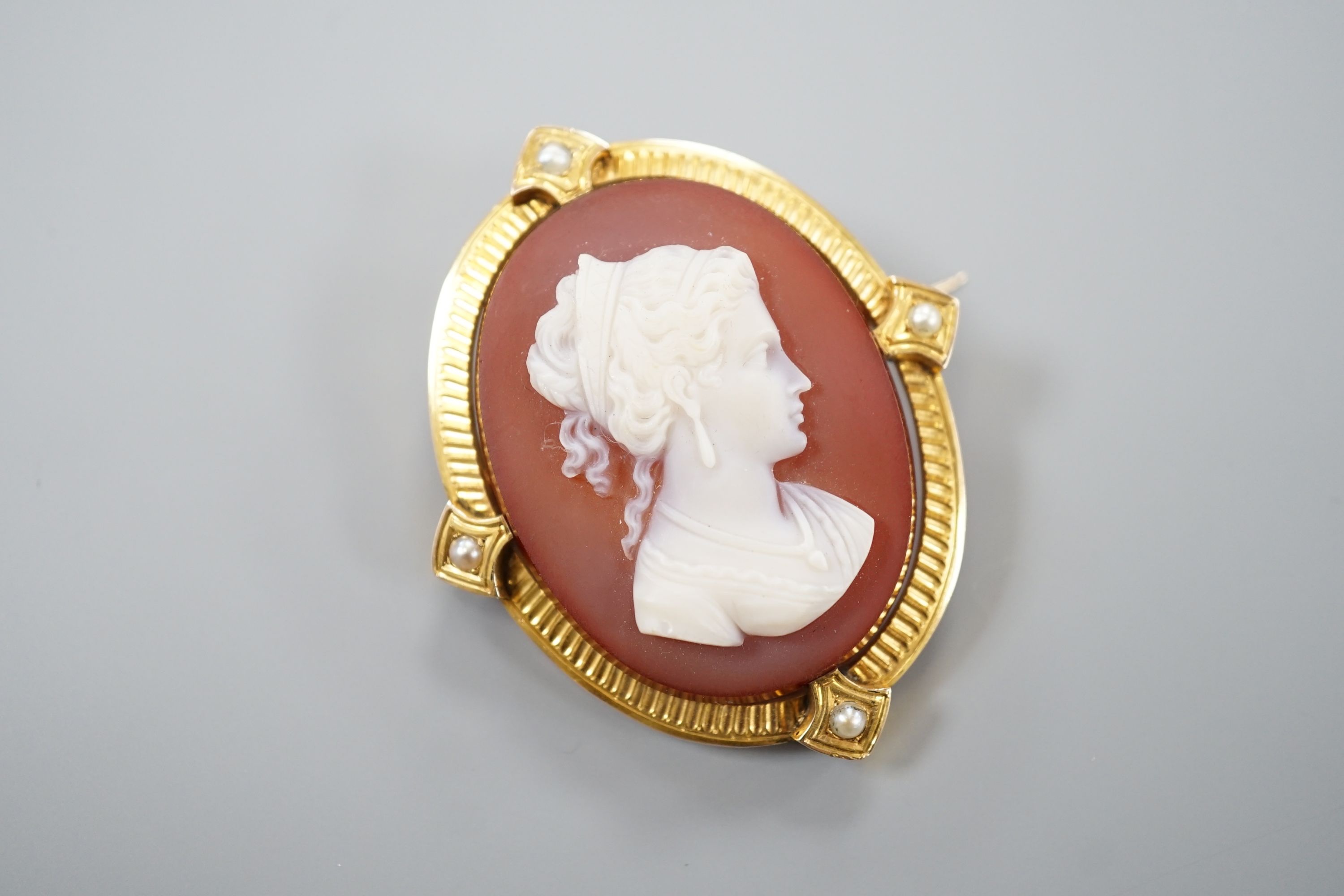 A late Victorian yellow metal and split pearl mounted oval sardonyx camel set brooch, carved with the bust of a lady to sinister, 47mm, gross 12.3 grams.